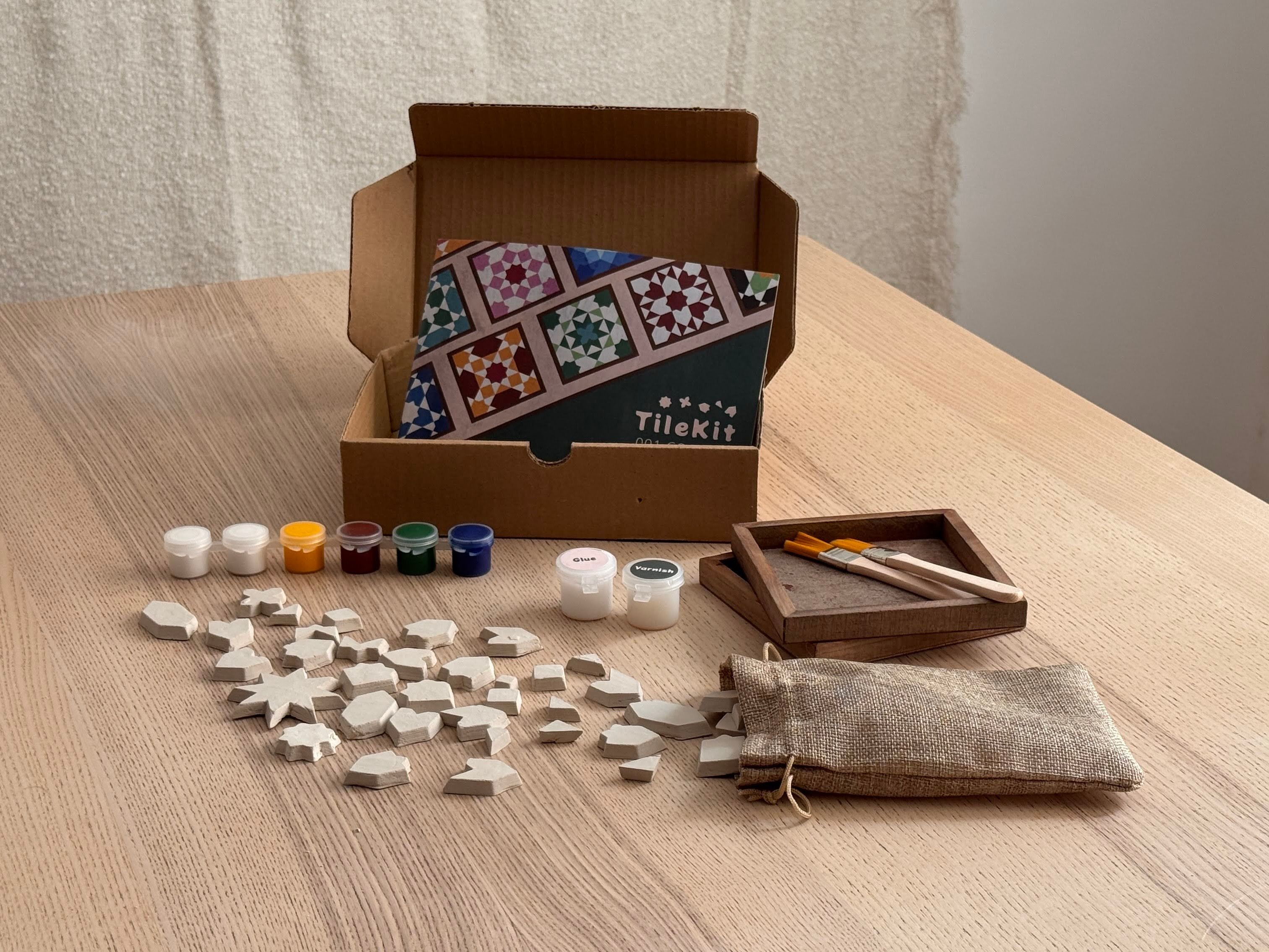 Geopende TileKit-doos op tafel met kleitegeltjes, verf, penselen en onderzetters